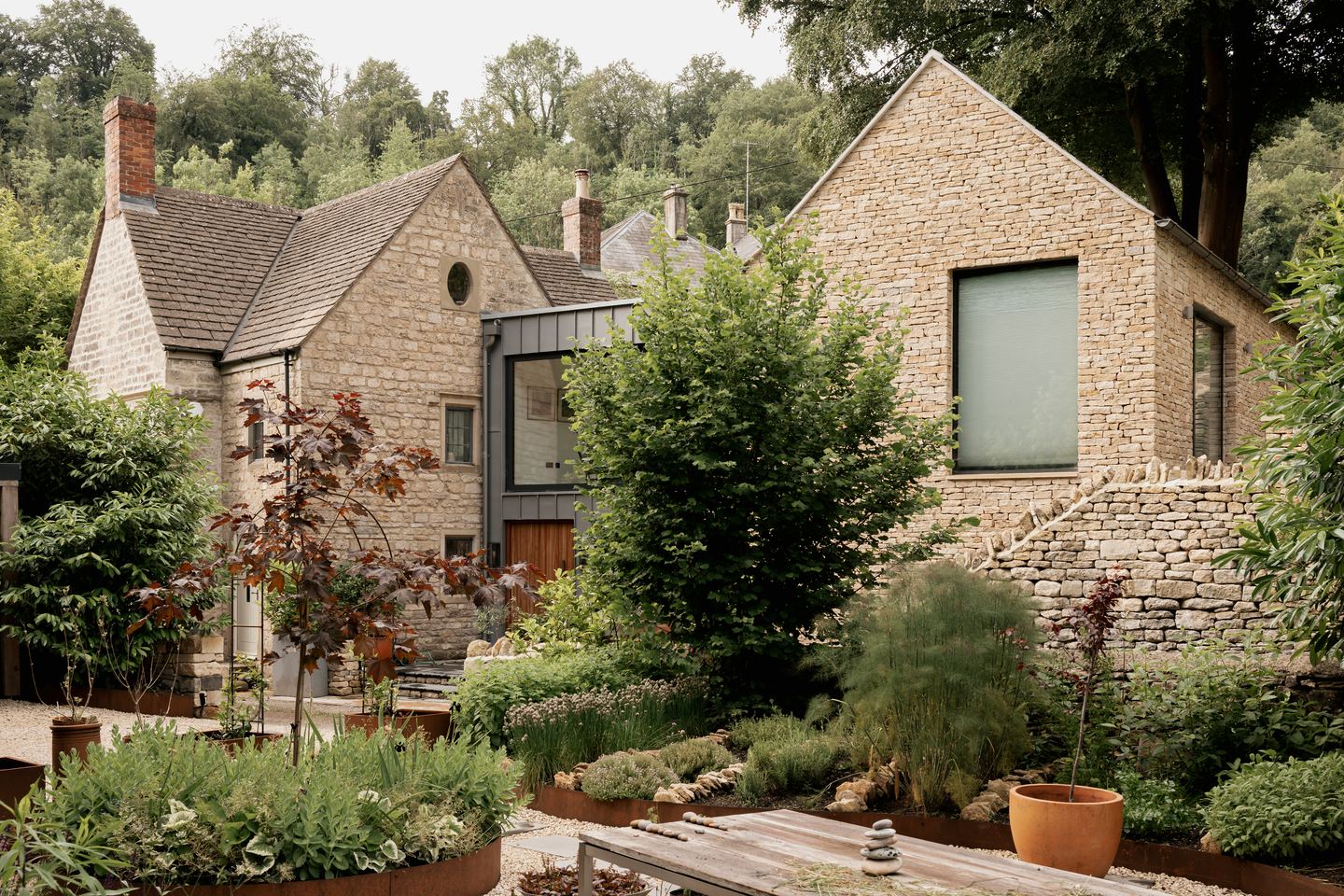 Cotswold Cottage Extension from the garden, listed stone cottage joined to a new dry-stone gable by a glazed zinc-clad link